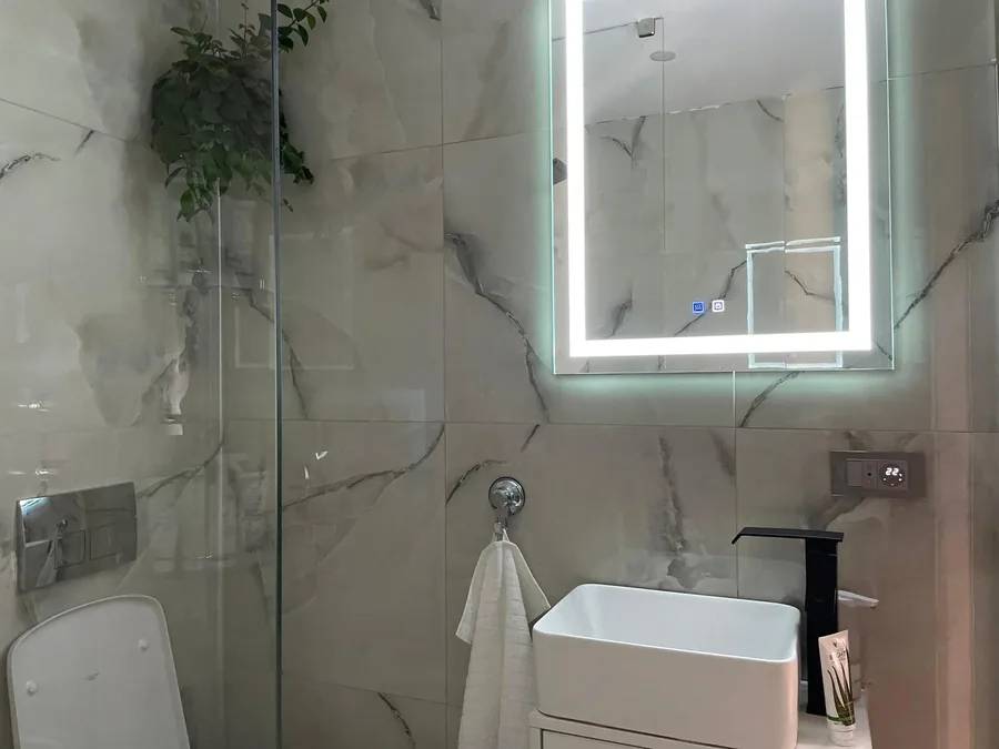 Elegant bathroom with light tiling, walk-in shower and LED mirror